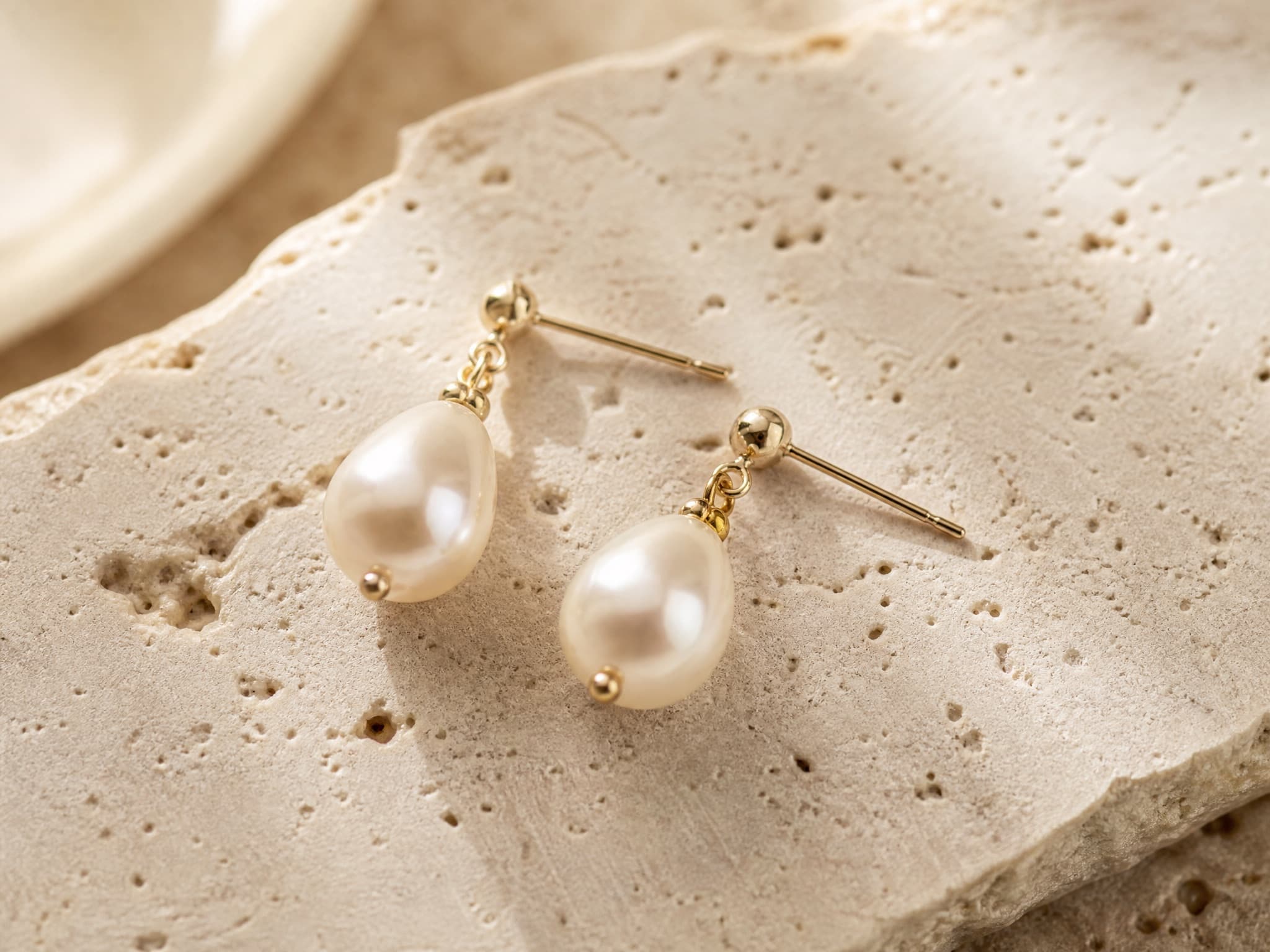 Pearl drop earrings, flat-lay on travertine